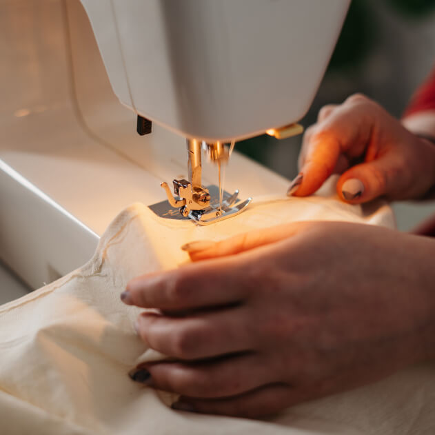 A person sewing a piece of clothing using a sewing machine.